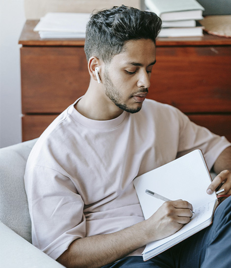 Man writing in a notebook looking very focused, represents how working with a ADHD specialist in Montclair, NJ can help you build on your strengths.