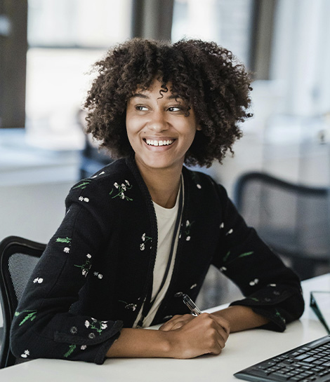 Smiling woman at her office desk, represents how working with an adult therapist in Montclair, NJ can help with challenges at work, relationships, parenting, stress, and more.